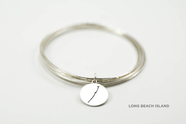 Stack of sterling silver hammered bangles featuring round Long Beach Island border with matte finish.