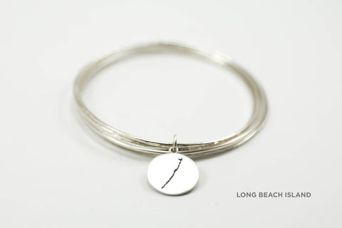 Stack of sterling silver hammered bangles featuring round Long Beach Island border with matte finish. 